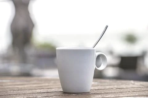 White cup of coffee with spoon on the table outdoors. Selective focus Stock Photos