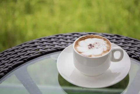 A white cup of coffee on the table with a backdrop of rice fields. Stock Photos