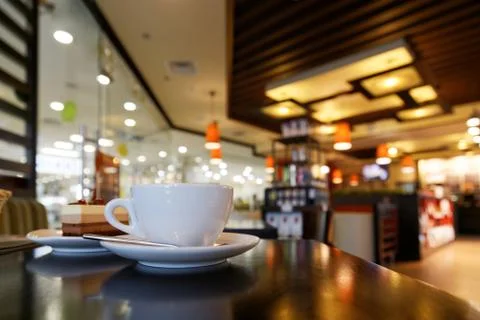 White cup of coffee on the table in coffee shop against blurred background Stock Photos