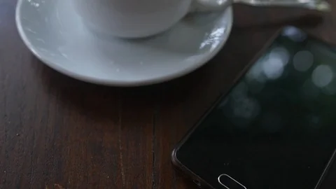 A white cup of coffee is on the table near the phone with a blurry reflection on Stock Footage 87208795