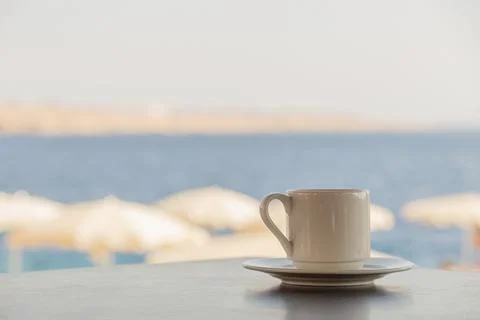 White cup of coffee on the table overlooking the beach with white umbrellas and Stock Photos
