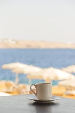 White cup of coffee on the table overlooking the beach with white umbrellas and Stock Photos