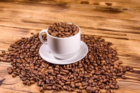 White cup filled with coffee beans on wooden table Stock Photos