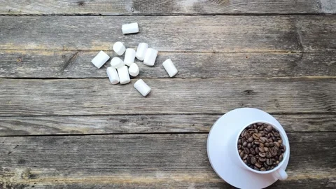White cup filled with roasted coffee beans on a wooden surface makes Stock Footage 303521156
