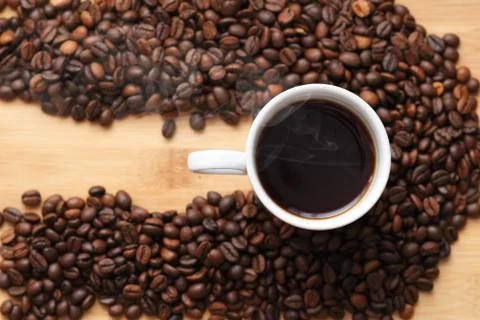 White Cup with hot coffee surrounded by coffee beans on wooden surface. with  Foto stock