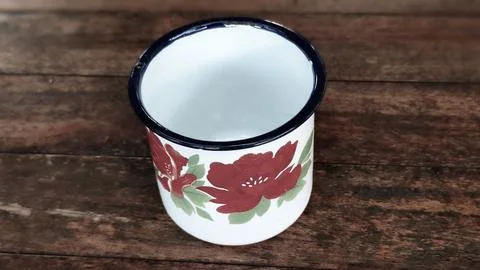 A white cup with a red flower design sits on a wooden table Stock Photos