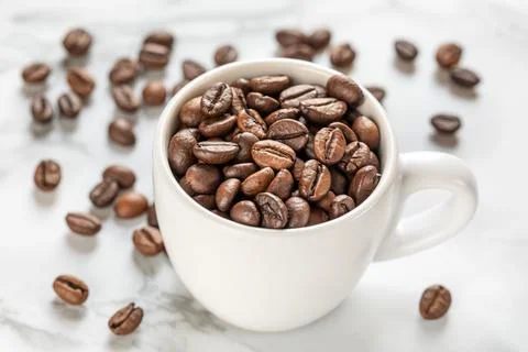 White cup with roasted coffee beans close up, white background. Good mood Stock Photos