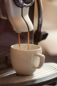 White cup standing on the grating of coffee machine with coffee pouring in th Stock Photos