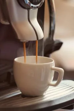 White cup standing on the grating of coffee machine with coffee pouring in th Stock Photos