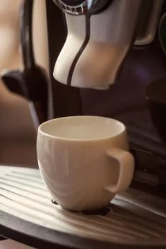 White cup standing on the grating of coffee machine with coffee pouring in th Stock Photos