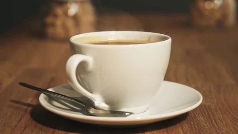 White cup of steaming hot coffee drink on saucer upon wooden table Stock Footage 72318675