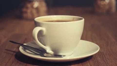 White cup of steaming hot coffee drink on saucer upon wooden desk Stock Footage 72318727