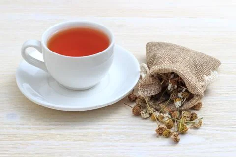 White cup of tea with chamomile in a pouch on a white wooden background Stock Photos
