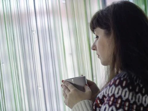 White cup with tea in the hands of a young woman standing by the window Stock Photos