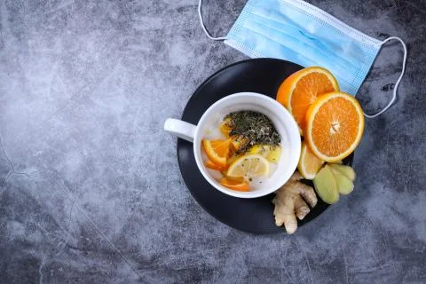 White cup of tea with lemon, ginger, orange, jam on the dark grey background. Stock Photos