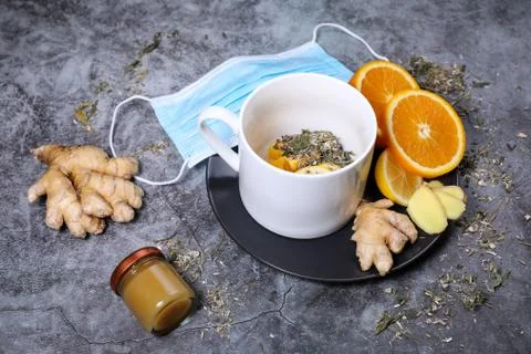 White cup of tea with lemon, ginger, orange, jam on the dark grey background. Stock Photos