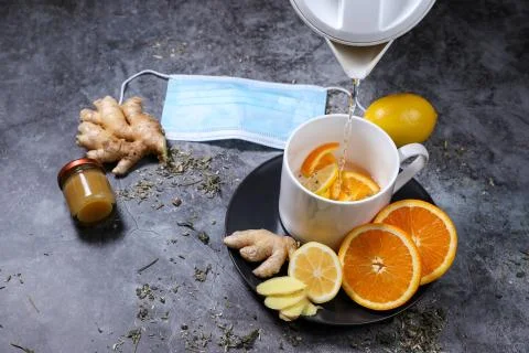 White cup of tea with lemon, ginger, orange, jam on the dark grey background. Stock Photos