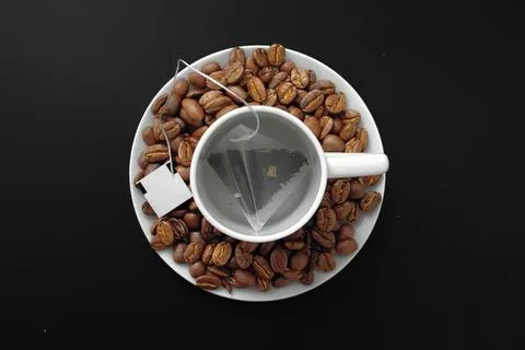 White cup of tea surrounded by coffee beans on black background Stock Photos