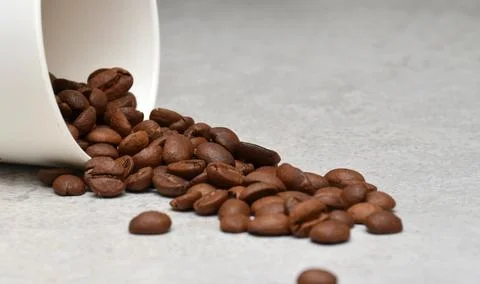 White cup from which coffee beans fall. Stock Photos