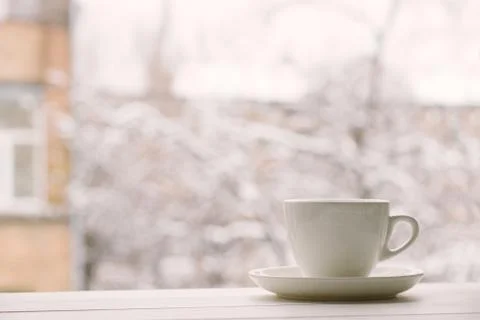 White cup in window sill on a background of house and snowy weather. Stock Photos