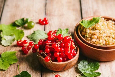 White currant and red currant with leaves in wooden bowls on a wooden backgro Stock Photos