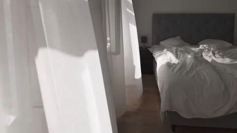 White curtain flying by the wind next to an unmade empty bed Stock Footage 313256336