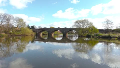 White delivery van crossing stone arch bridge over calm river with bright sky Video stock 343756881