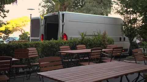 White delivery van with open rear doors parked beside an empty outdoor cafe.. Stock Footage 342037130