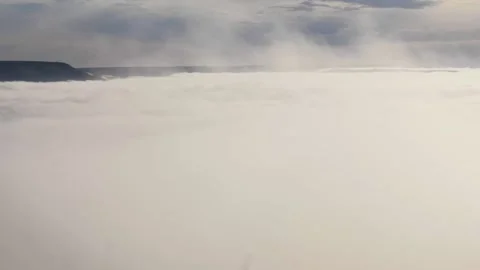 White dense fog from which the tops of flat hills are visible under the blue sky Stock Footage 241565762