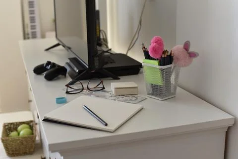 White desk open notebook pencil eyeglasses colored pencils pom-poms high-angle Foto stock
