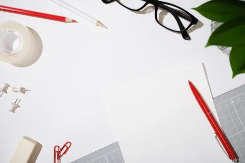 White desk with workspace essentials. Blank paper, red pen, glasses, and of.. Фото