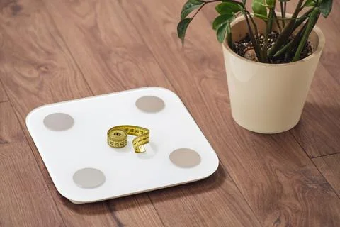 White digital bathroom scale with yellow measuring tape on wooden floor bes.. Stock Photos