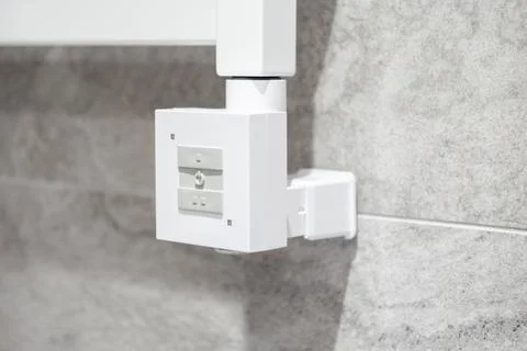 A white digital heating controller for a bathroom radiator attached to a gray Stock Photos