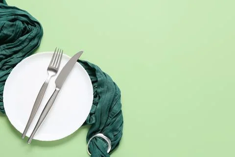 White dinner plate with modern silverware and a dark green napkin on a light  Stock Photos