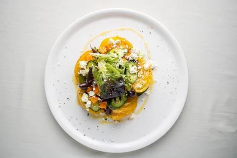 White dinner plate with a vibrant array of vegetables and a creamy sauce garnish Stock-Fotos