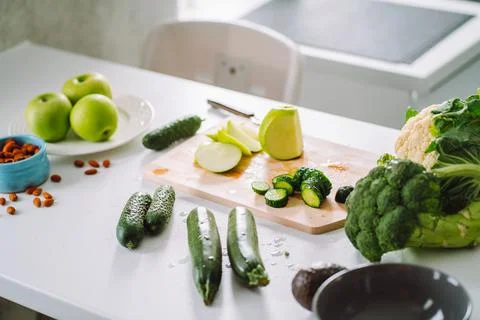 White dinner table with green vegetable on cutting board in light kitchen Foto stock