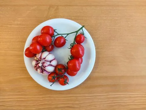White dish with bunch of mini tomatoes and garlic. Stock Photos