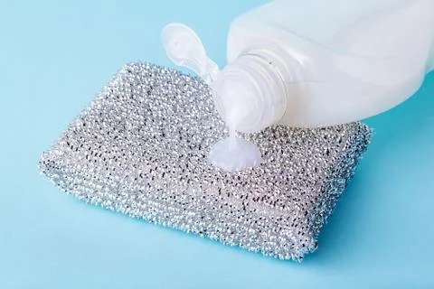 White dishwashing liquid flows from a plastic bottle onto silver foam sponge. Stock Photos