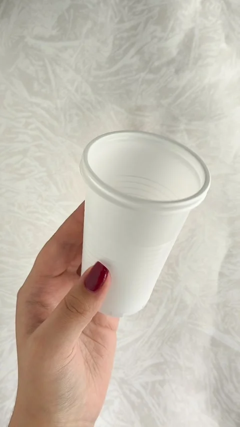 White disposable plastic cups for drinks in a womans hand. The use of disposable Stock Footage 317093661