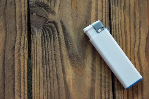 A white disposable plastic lighter is positioned on a wooden background. Top Stock Photos