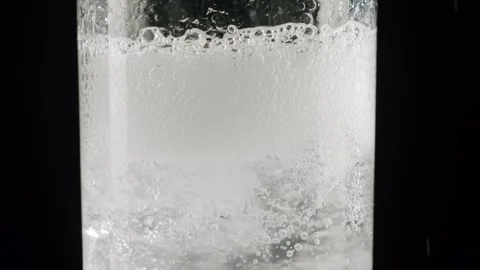 White dissolving pill creating fizzy bubbles in dark liquid Stock Footage 342736920