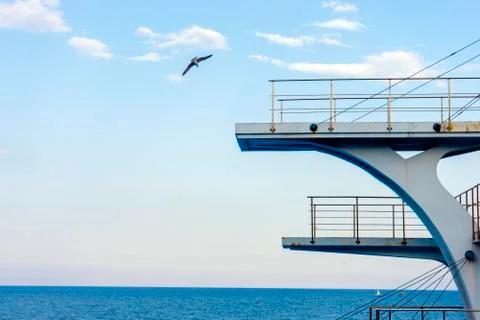 White diving board or tower against a clear blue sky. In the background the s Stock Photos