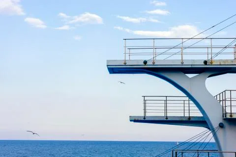 White diving board or tower against a clear blue sky. In the background the s Stock Photos