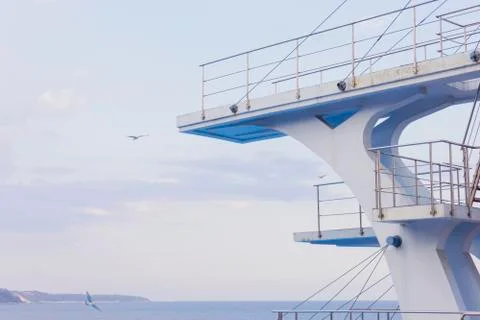 White diving board or tower against a clear blue sky. In the background the s Stock Photos