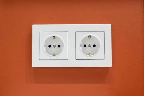 White double electrical socket on orange wall providing electricity Stock-Fotos