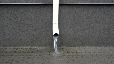 A white drainpipe on the front of the building pours a stream of water the rain Video stock 118511507