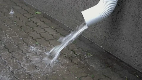 A white drainpipe on the house pours a stream of water onto the paving slabs  Video stock 116439589