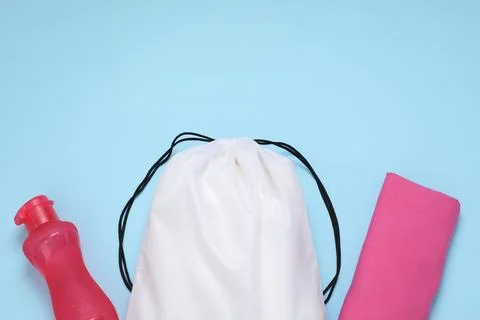White drawstring bag, bottle and cloth on light blue background, flat lay. .. Foto stock