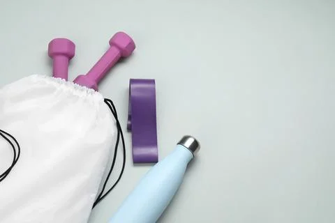 White drawstring bag, thermo bottle, fitness elastic band and dumbbells on .. Stock Photos