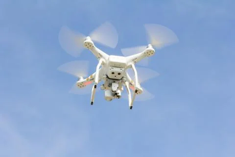 White drone hovering in a bright blue sky. Stock Photos